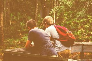 Two friends, side by side, facing a forest. Mental health support.