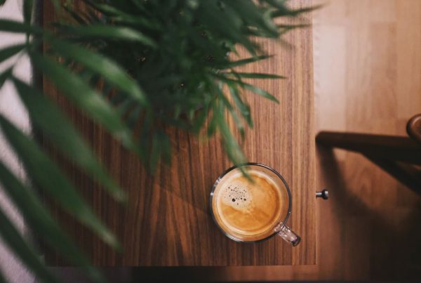 half-filled coffee in clear glass mug beside plant on brown table photo