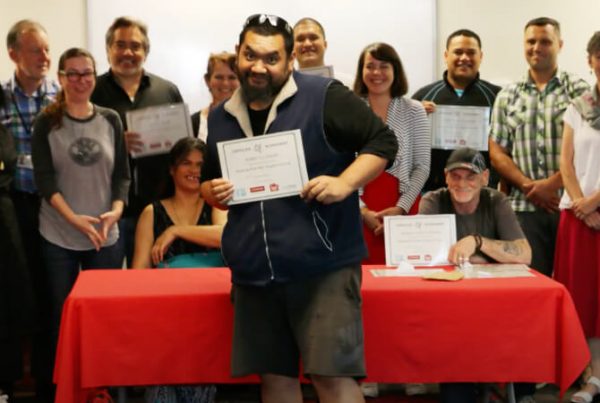 A group of Peer Support workers at their training graduation ceremony; one of the graduates is in the foreground, holding up his certificate proudly.