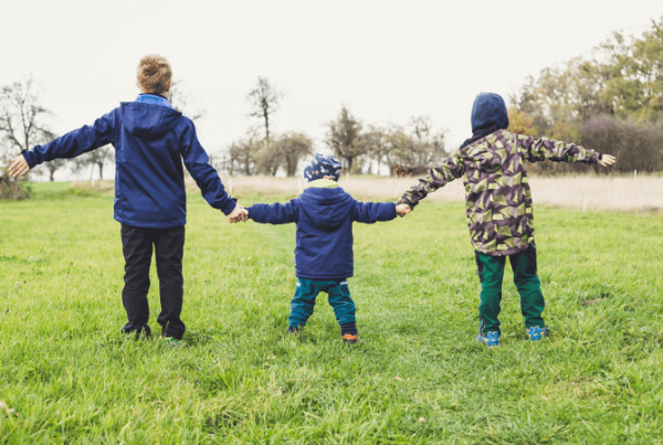 Three children holding hands in a field, with their arms wide open. Photo by Markus Spiske on Unsplash