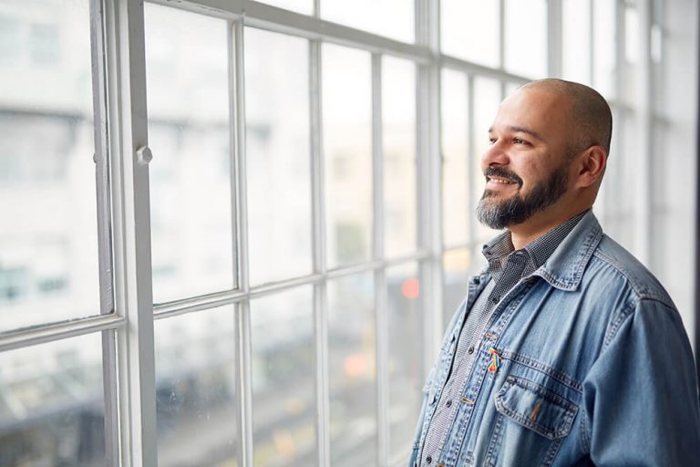 Kind-looking bearded man in denim jacket gazing out of a window