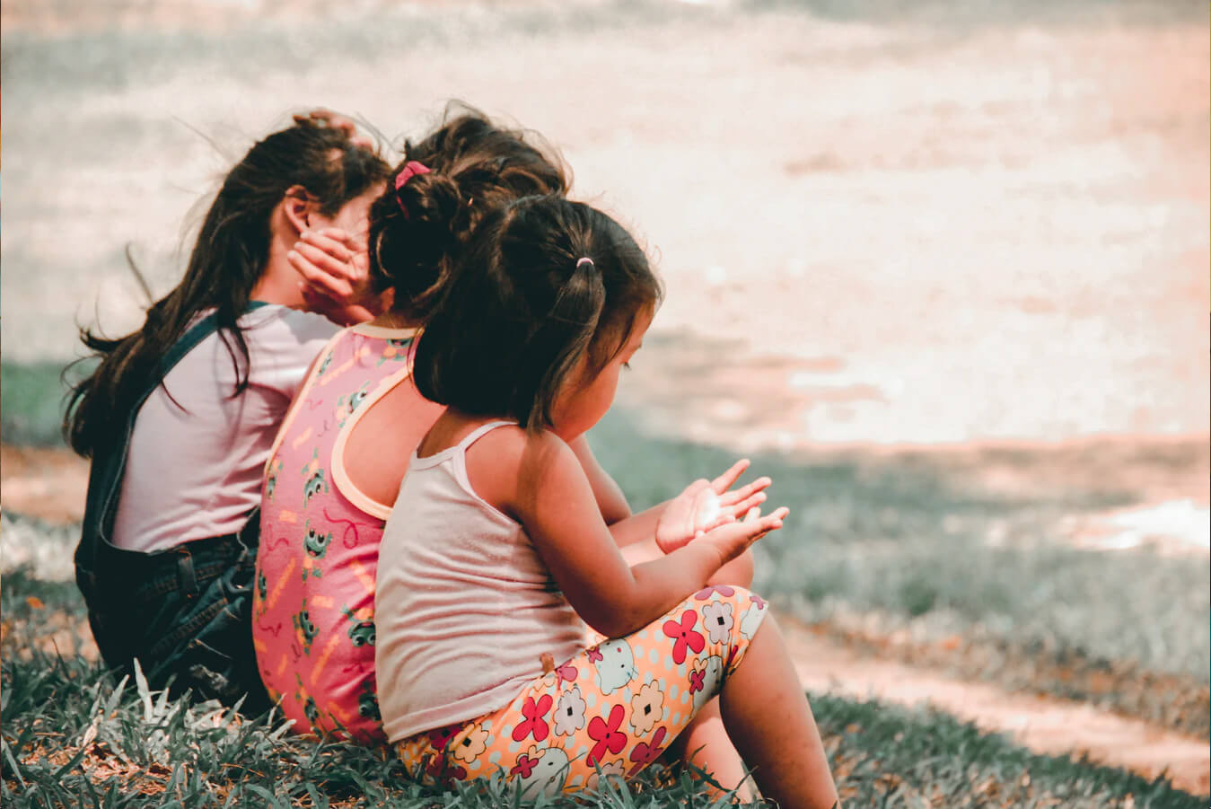 Three little girls sitting together on a grassy bank.