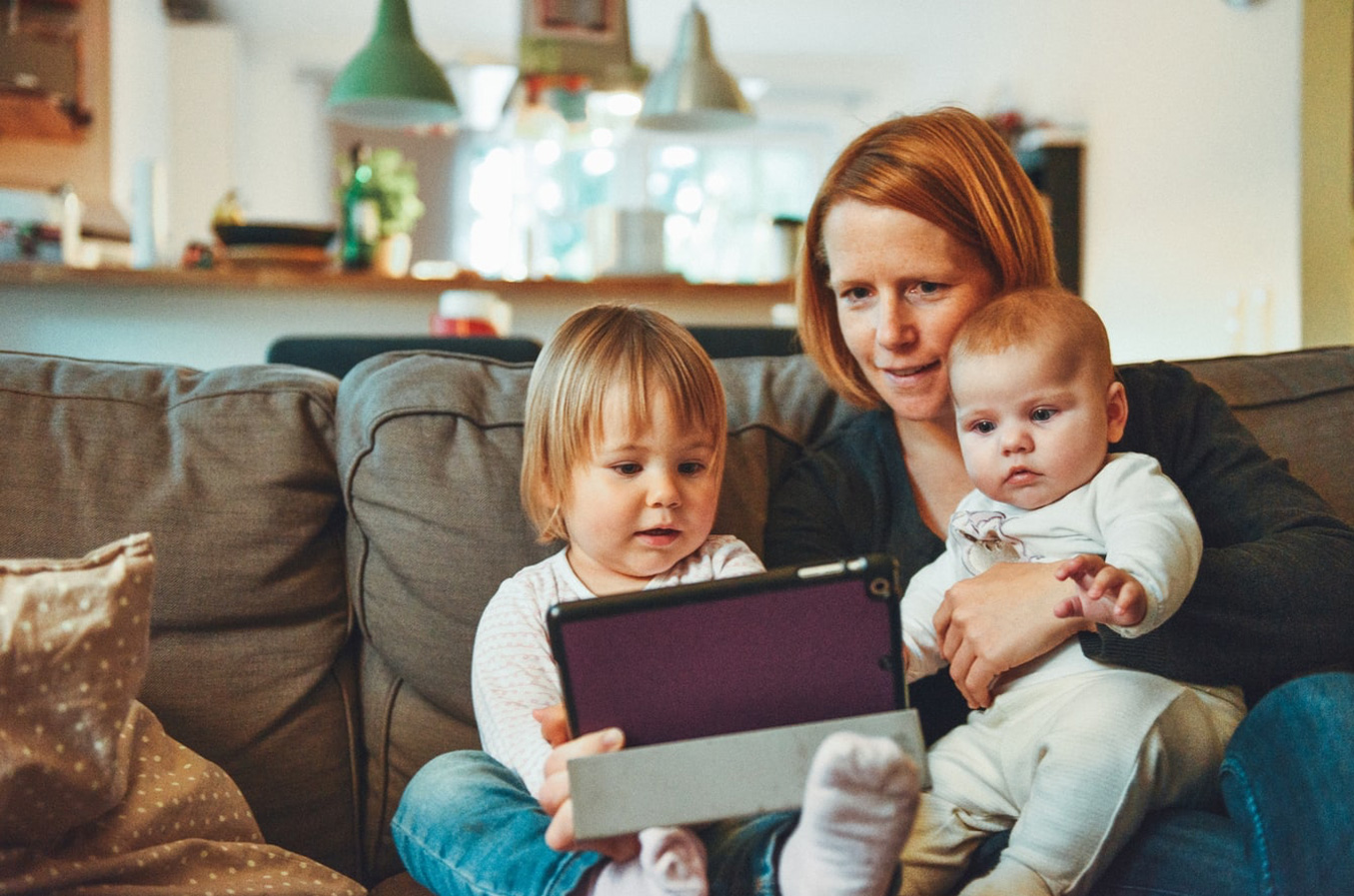 A mother sitting with her baby and toddler, watching a parenting seminar from home
