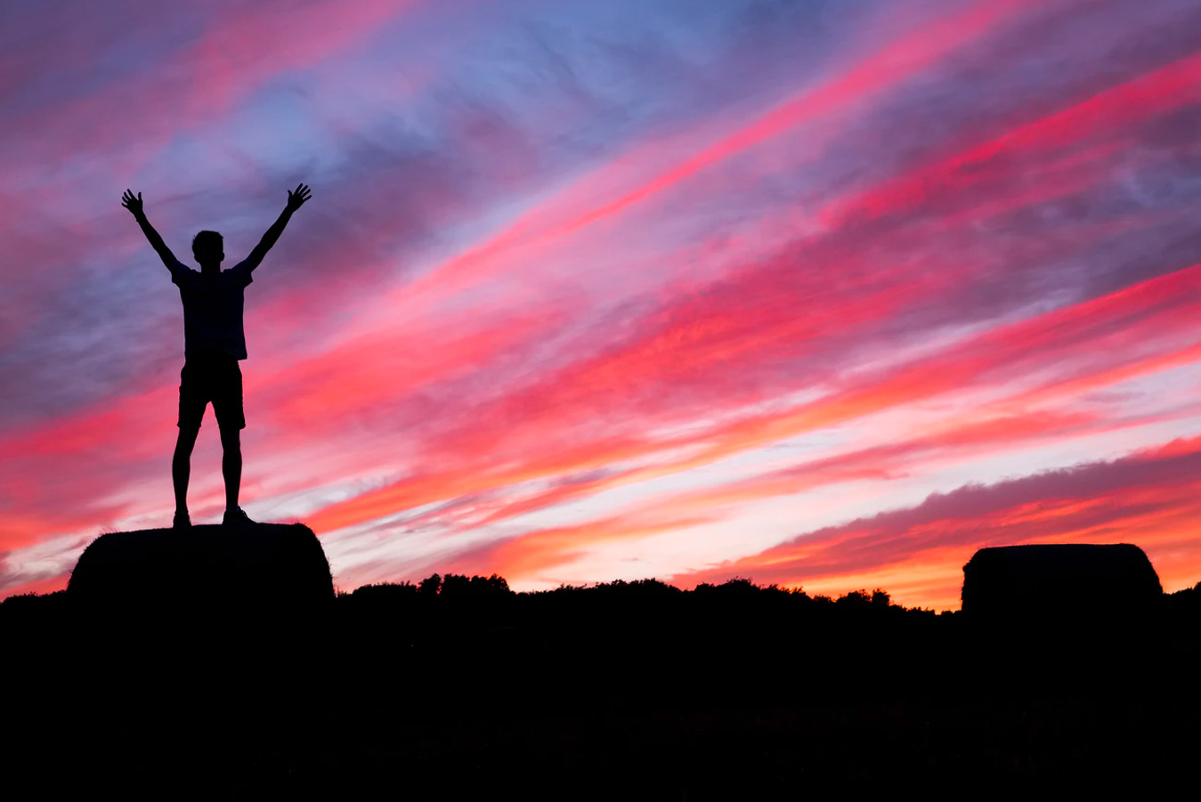 Black foregrond with a person standing, arms raised in success against a sunset backdrop