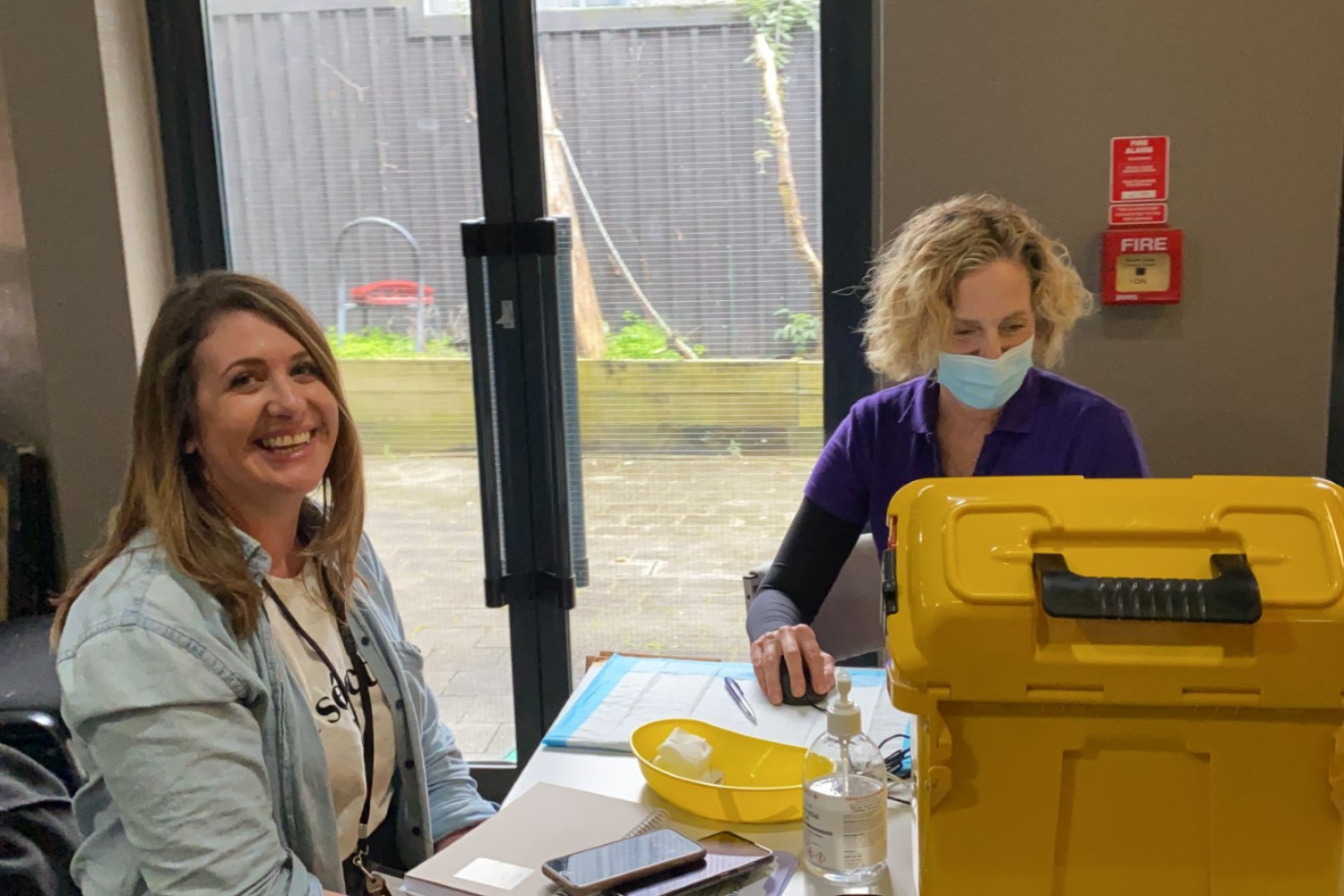 Smiling woman, sitting at a table with a nurse, waiting to get her vaccine shot.