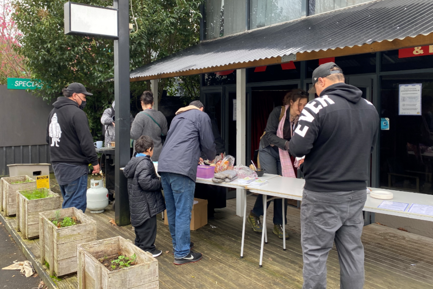 A group of people setting up food on trestle tables outside a motel.