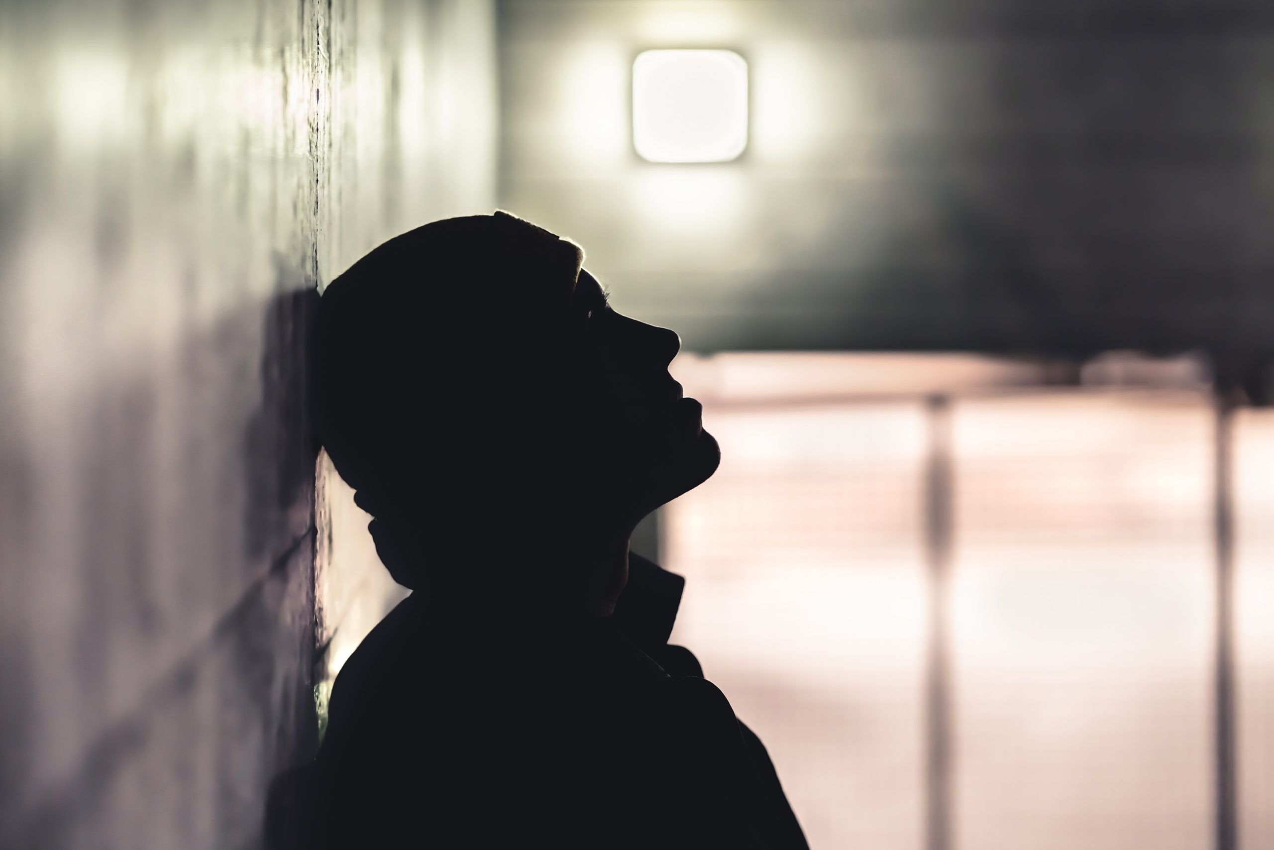 Silhouette of a teen boy slumped against a brick wall